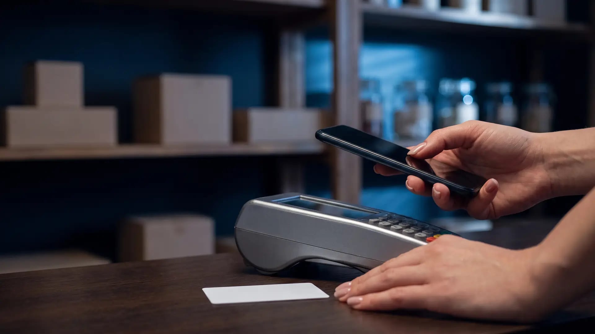 A shopper tapping a smartphone against a plain unbranded card terminal on a boutique counter in the Gulf